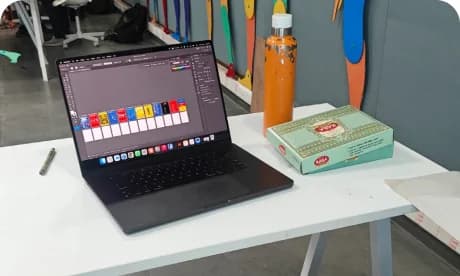 Saaraj's desk with a laptop, a colour swatch card and a drink