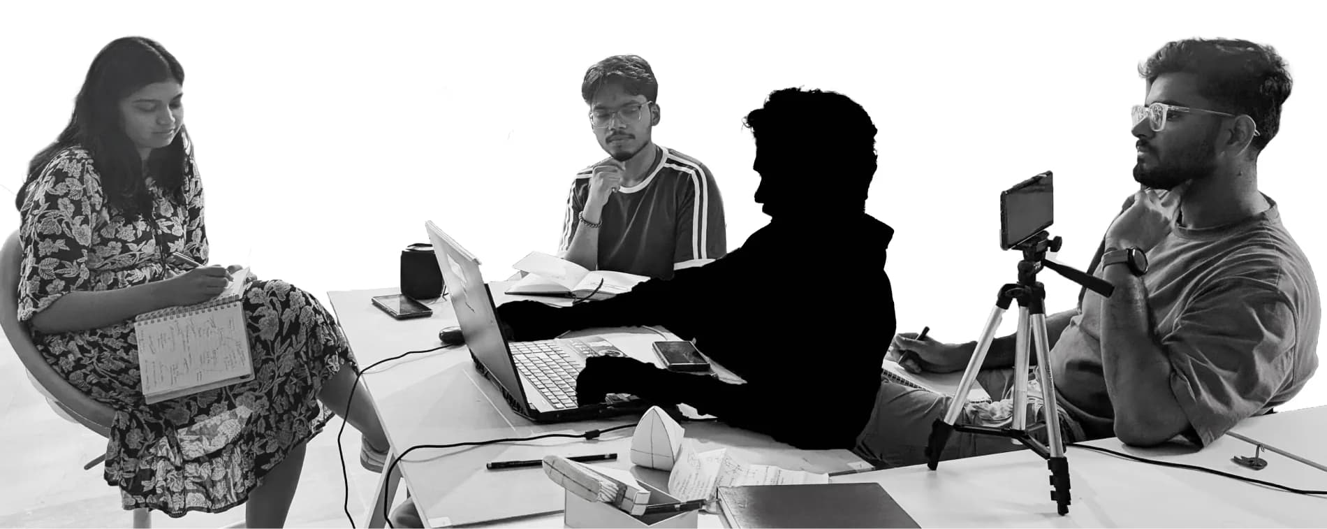 The three researchers seated around a table with laptops, notebooks and a camera on a tripod