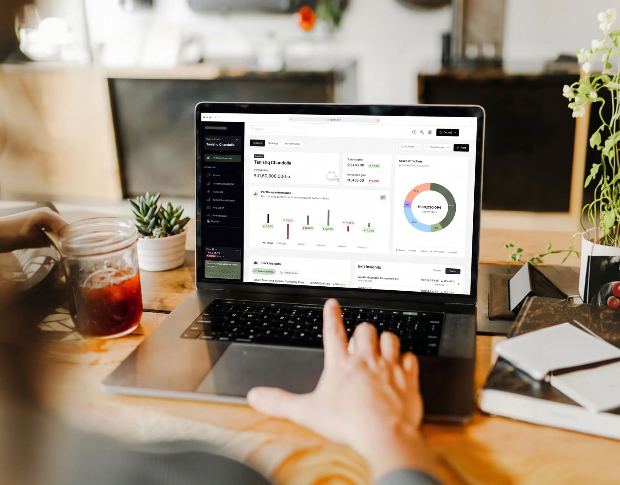 Laptop on a desk showing the investments tracking dashboard, next to a plant and an iced coffee
